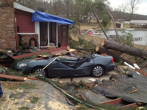 car destroyed and trees toppled in front of a house from storm damage